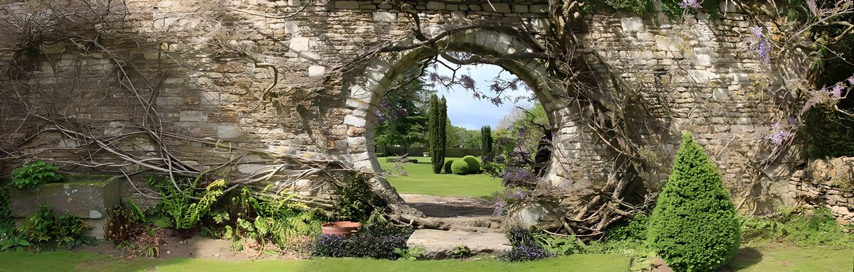 OCUK12242: Long brick wall covered with branches and with a round passage to the garden